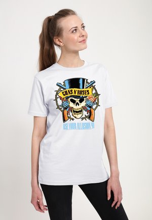 Ung kvinde iført en hvid Guns N’ Roses t-shirt med kranium, krydsede pistoler, høj hat og "Use Your Illusion 91" tekst.