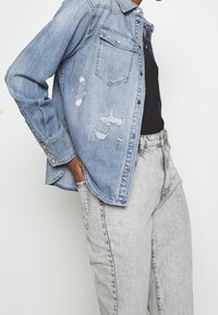 Koszula dżinsowa, jasnoniebieska, z kieszonką na piersi i przetarciami. Połączona z wysokim stanem, wyblakłymi szarymi dżinsami. Gładka bawełniana tekstura.