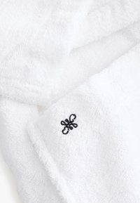Tissu blanc doux avec un petit symbole décoratif noir brodé sur le bord plié d'une serviette ou d'un peignoir.