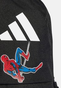 Czarna nylonowa plecak z dużym białym logo adidas oraz kolorową naklejką z postacią Spider-Mana w czerwono-niebieskich odcieniach.