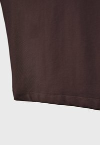 Donkerbruin stof met zichtbare stiksels langs de onderste zoom, met een gladde textuur en lichte plooien.