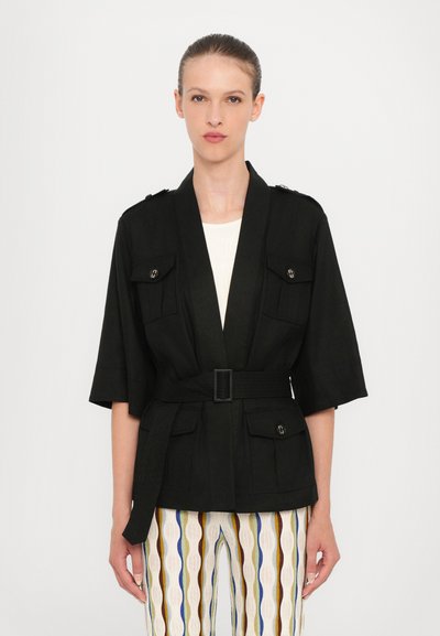 Zwarte blazer met korte mouwen, twee voorkzakken en schouderaccenten. Gecombineerd met gestreepte, veelkleurige broeken.