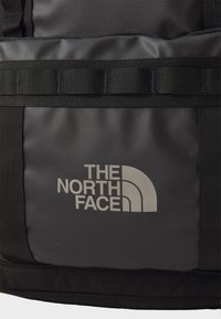 Musta reppu, jossa on kestävä kangas, säädettävät hihnat ja näkyvä hopeinen The North Face -logo tekstuuripaneelissa.