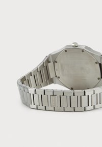 Montre en acier inoxydable argenté avec un boîtier octagonal et un bracelet à maillons. Présente une finition mate et des détails gravés au dos.