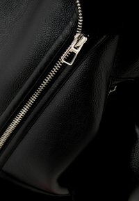 Czarna torebka z fakturalnej skóry z wyraźnym srebrnym zamkiem błyskawicznym i pętelką do jego otwierania, przedstawiająca zbliżenie na zamykaną na zamek kieszeń.