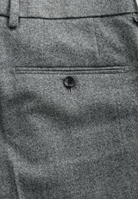 Graue Stoffhose mit feiner Textur, ausgestattet mit einer einzelnen Gesäßtasche mit einem schwarzen Knopfverschluss und einem flachen Vorderdesign.