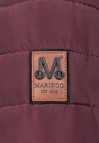 Tejido sintético de color burdeos oscuro con un parche de cuero que presenta un logo en relieve y el texto "MARIKOO EST 2016", bordeado por tela negra.