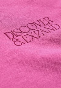 Tessuto di cotone rosa con testo impresso che recita "SCOPRI E ESPANDI". La texture è liscia con una finitura leggermente opaca.