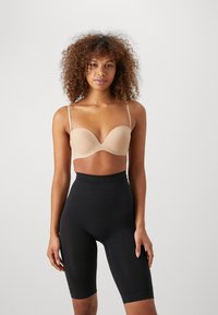 Beige molded bra with adjustable straps, smooth texture, and low-cut design, paired with high-waisted black smoothing shorts.