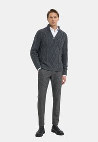 Maglione grigio a maglia con motivo a diamante, colletto a mezza zip, indossato sopra una camicia bianca, abbinato a pantaloni grigi strutturati e stivali neri.