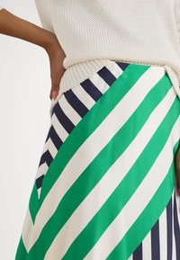 Saia multicolor com riscas diagonais verdes, brancas e azuis marinho. O tecido tem uma textura suave, combinado com um top branco em malha.