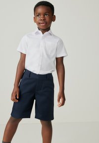 Witte korte mouwen shirt met een zak, gecombineerd met marineblauwe shorts. Het shirt heeft knoopsluitingen en een gladde textuur.