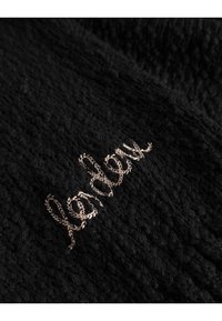 Czarna, teksturowana tkanina z haftowanym, kursywnym wzorem w jasnobrązowym kolorze, który wyraża słowo "lender". Całkowita powierzchnia wydaje się puszysta.