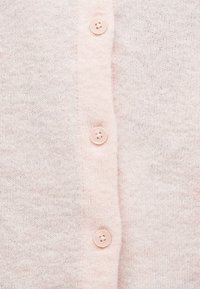 Μαλακό ροζ πλεκτό ύφασμα με τρία διάφανα ροζ κουμπιά ευθυγραμμισμένα κατακόρυφα στο κέντρο.