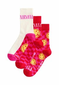Drei Paar Socken: ein weißes Paar mit pinkem "NIRVANA"-Schriftzug und zwei rote mit gelben smiley Gesichtern und einem pinken Schachbrettmuster.