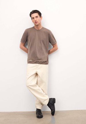 T-shirt marron à manches courtes associé à un pantalon beige ample et des chaussures noires. Design simple avec des couleurs neutres et un style minimaliste.