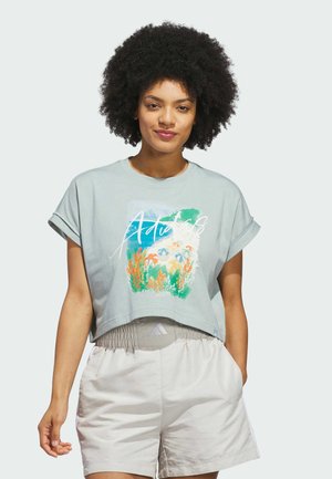 Jasnoniebieska krótka koszulka z podwiniętymi rękawami, z kolorową grafiką natury i napisem "Adidas". Do niej dopasowane jasne szorty.