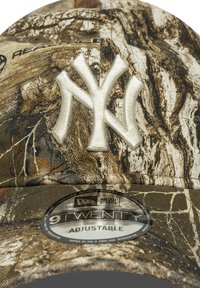 Gorra de béisbol con estampado de camuflaje y un logotipo de Nueva York bordado en blanco, hecha de un tejido con acabado texturizado. Cuenta con una correa ajustable.
