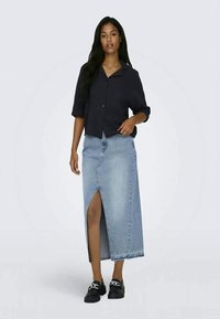 Camisa escura de botões, saia maxi de ganga azul claro com fenda frontal, feita de material suave, usada com sapatos de plataforma pretos.