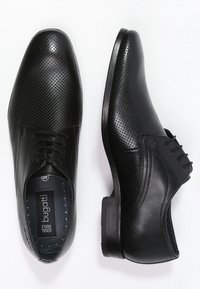 Chaussures en cuir noir avec un design perforé et des accents lisses. Fermeture à lacets et talon bas. L'intérieur affiche l'étiquette de la marque.