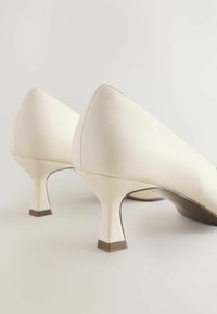 Zapatos de tacón alto de cuero blanco con puntera puntiaguda y diseño de tacón hexagonal, con una textura suave y acentos mínimos.