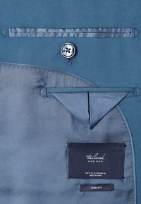 Blaues maßgeschneidertes Jacket-Innenfutter aus glattem Stoff, mit einem Knopf und einem Etikett mit Pflegehinweisen und Größenangaben.