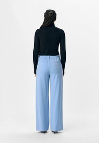Schwarzer Rollkragenpullover, tailliert, kombiniert mit weit geschnittenen, hellblauen Hosen mit elastischem Bund und Gesäßtaschen.