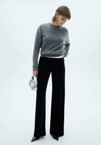 Maglione grigio a maglia, pantaloni neri a vita alta con gamba larga, tacchi neri a punta e una borsa metallizzata argentata con design arricciato.
