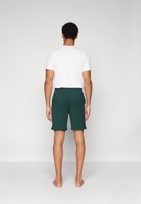 Groene shorts van zachte stof, met een elastische tailleband en zijzakken. Draagt een witte t-shirt met ronde hals.