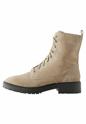 Bottines en daim beige avec un bout arrondi et un laçage à l'avant. Présente une semelle en caoutchouc noir résistante et un talon en boucle pour un enfilage facile.
