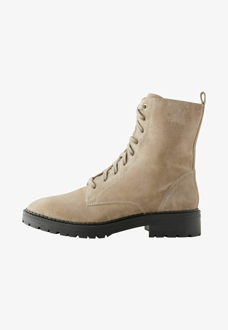 Botas de tobillo de ante beige con punta redonda y cierre de cordones. Cuenta con una suela de goma negra resistente y un talón en forma de lazo para ponerlas y quitarlas fácilmente.