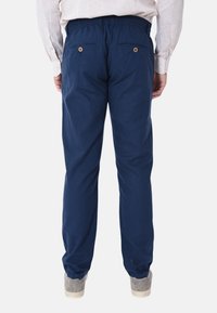 Pantaloni blu navy con cintura elasticizzata, dotati di due tasche posteriori con bottone. Realizzati in un tessuto morbido, dalla vestibilità ampia. Indossati con scarpe da ginnastica grigie.