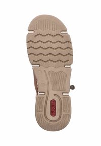 Semelle de chaussure marron avec une surface en caoutchouc beige texturé, présentant des motifs en zigzag, des crêtes et un logo rouge circulaire au centre.