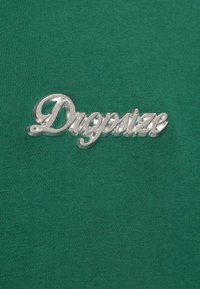 Grøn stof med en glat tekstur har et metalisk sølv "Dropsize" tekstlogo, skrevet med kursiv.