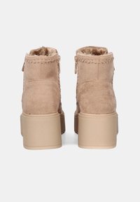 Botas de tobillo marrones con acabado de ante texturizado, cuentan con un ribete trenzado, cremalleras doradas y una suela de plataforma gruesa en color beige.