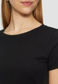 Melna kokvilnas T-kreklu ar apaļu kakla izgriezumu un īsām piedurknēm, tam ir gluda tekstūra un smalki izšuvumi.