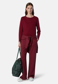 Sudadera de manga larga burdeos con textura de punto y logo, combinada con pantalones a juego con cinturilla atada. Bolsa de gimnasio verde con texto impreso.