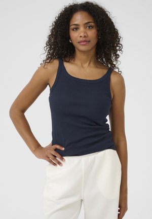 Marineblaues, geripptes Tanktop mit breiten Schulterträgern und einem Rundhalsausschnitt, kombiniert mit hellen, locker sitzenden Hosen. Weicher Stoff.