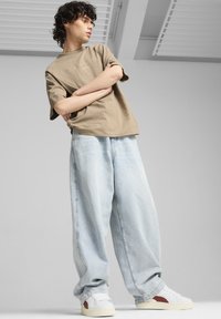 T-shirt beige in cotone con testo ricamato, abbinata a pantaloni in denim azzurro oversize. Sneakers bianche con dettagli rossi completano il look.
