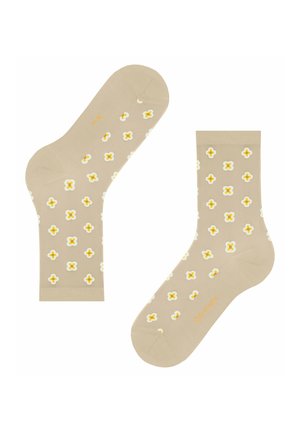 Beżowe skarpetki z powtarzającym się wzorem małych białych i żółtych czteropłatkowych kwiatów, z subtelnym pomarańczowym napisem marki na podeszwie i palcach.