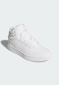 Biele vysoké tenisky s textúrovanou kožou a sieťovinovými akcentmi. Vlastnosti zahŕňajú perforovanú špičku, prešívané detaily a ploché šnúrky. Branding na boku.