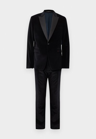 Μαύρο βελούδινο ταγέρ με σατέν πέτα, σακάκι με ένα κουμπί και ταιριαστά ραμμένα παντελόνια σε απλό φόντο.