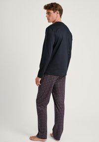 Marineblauw overhemd met lange mouwen, gecombineerd met een pyjamabroek met een patroon van kleine rood-witte geometrische ontwerpen, gemaakt van zachte stof.