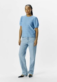 Ljusblå broderad blus med puffärmar, parat med ljusblå rakbenade jeans och svarta spetsiga klackar.
