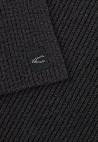 Donkergrijze ribbelstof met een zachte textuur. Een zwart vierkant patch met een logo is zichtbaar in een van de hoeken.