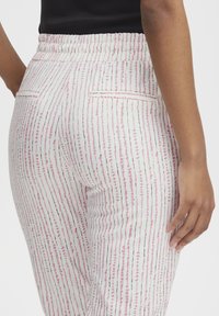 Witte broek met een verticale roze en zwarte gestreepte patroon. Voorzien van een elastische tailleband en twee achterzakken. Glad van textuur.