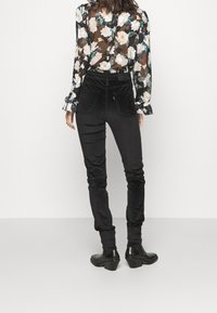 Pantalones ajustados de terciopelo negro con cintura alta, que presentan una textura suave y un diseño ceñido, combinados con una blusa de tul floral.