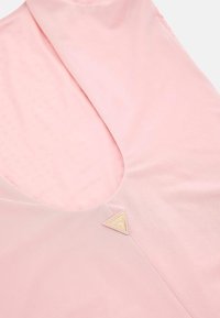 Rožinė audinė palaidinė su giliu V formos iškirpimu, lengva tekstūra ir trikampiu auksiniu logotipu su žodžiu "GUESS."