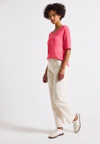 Rosa v-hals t-shirt med korte ærmer, parret med lyse beige lige ben bukser og крем sneakers med brune detaljer.