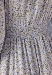 Bloemige jurk van lichte stof met een klein blauw en groen bloemenpatroon, gerimpelde tailleband en geplooide details bij de zoom.